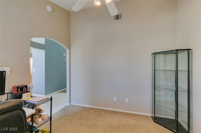 carpeted office space with ceiling fan and a towering ceiling