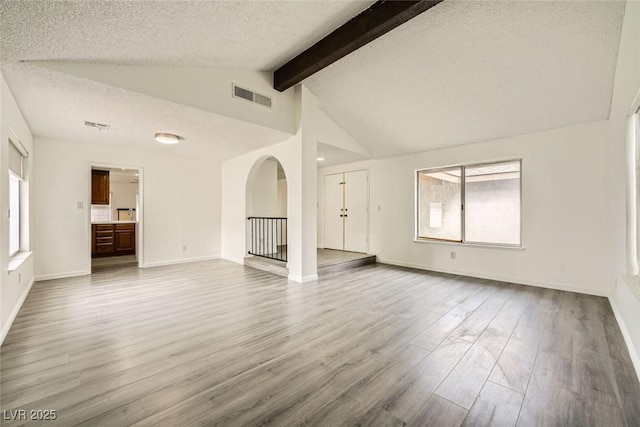 unfurnished living room with hardwood / wood-style flooring, lofted ceiling with beams, and a textured ceiling