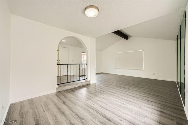 empty room with hardwood / wood-style floors, vaulted ceiling with beams, and a textured ceiling