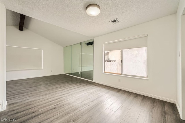 unfurnished bedroom with lofted ceiling, wood-type flooring, a closet, and a textured ceiling