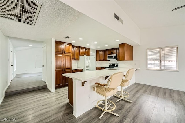 kitchen featuring stainless steel appliances, kitchen peninsula, a breakfast bar area, and light wood-type flooring