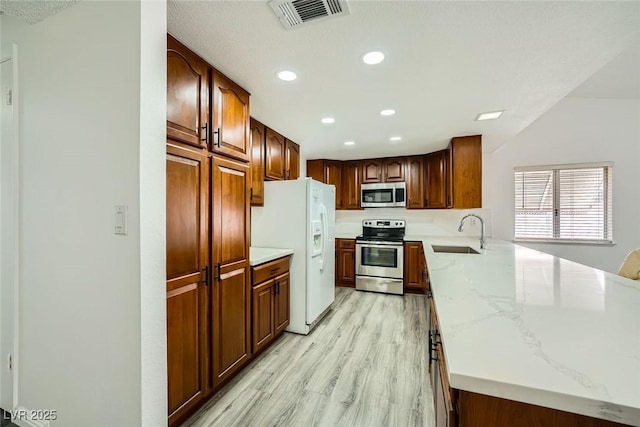 kitchen with light stone counters, appliances with stainless steel finishes, light hardwood / wood-style floors, and sink