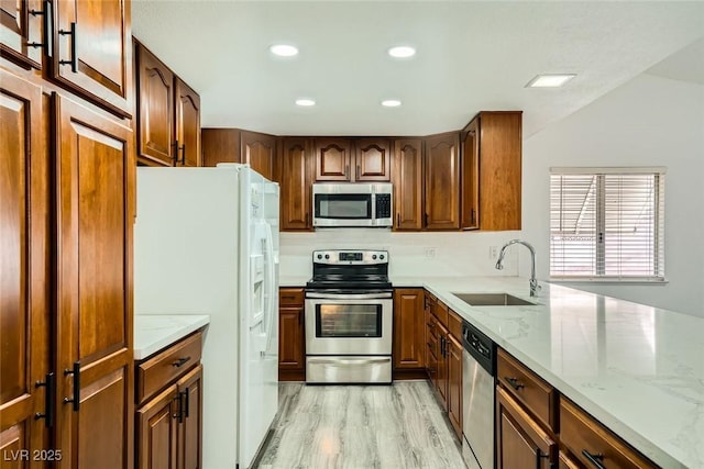 kitchen featuring lofted ceiling, sink, stainless steel appliances, light stone countertops, and light wood-type flooring