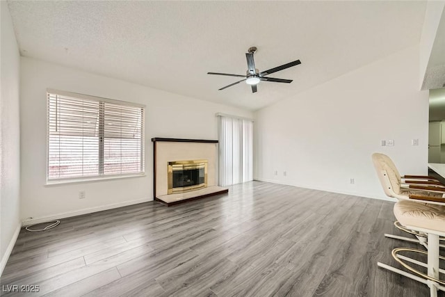 unfurnished living room featuring hardwood / wood-style flooring, ceiling fan, vaulted ceiling, and a textured ceiling