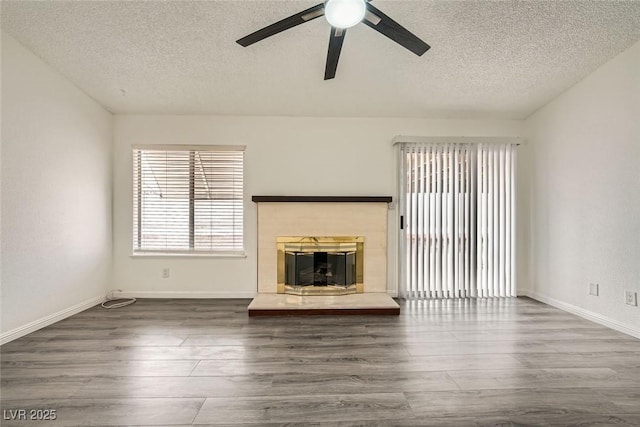 unfurnished living room with ceiling fan, dark hardwood / wood-style flooring, a tile fireplace, and a textured ceiling