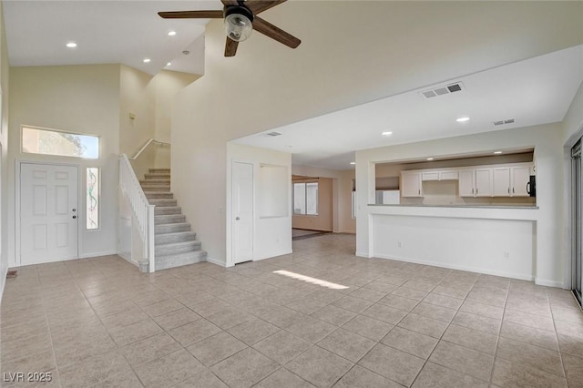 unfurnished living room with light tile patterned floors, a towering ceiling, and ceiling fan