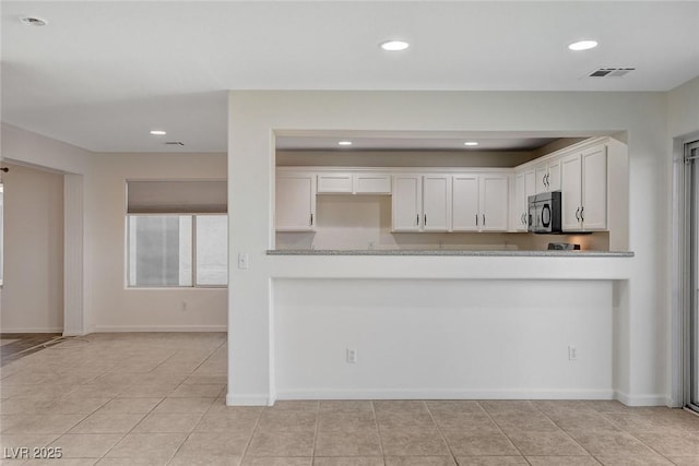 kitchen with white cabinetry, light tile patterned flooring, light stone counters, and kitchen peninsula