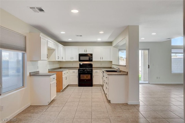 kitchen featuring white cabinetry, sink, dark stone counters, light tile patterned floors, and black appliances