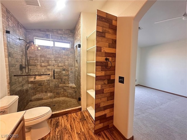 bathroom featuring a shower with door, ceiling fan, vanity, wood-type flooring, and toilet