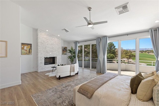 bedroom with lofted ceiling, light hardwood / wood-style flooring, ceiling fan, a stone fireplace, and access to outside