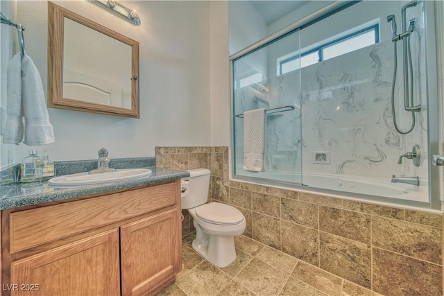 full bathroom featuring tiled shower / bath, vanity, toilet, and tile walls