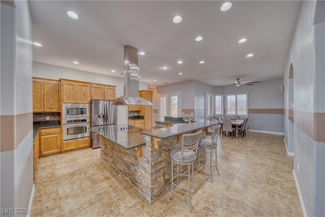 kitchen featuring appliances with stainless steel finishes, a breakfast bar, island range hood, a large island, and ceiling fan