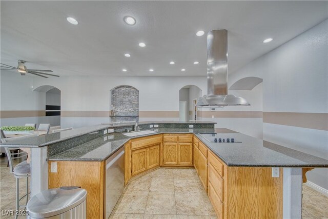 kitchen featuring sink, dishwasher, dark stone countertops, island range hood, and a kitchen bar