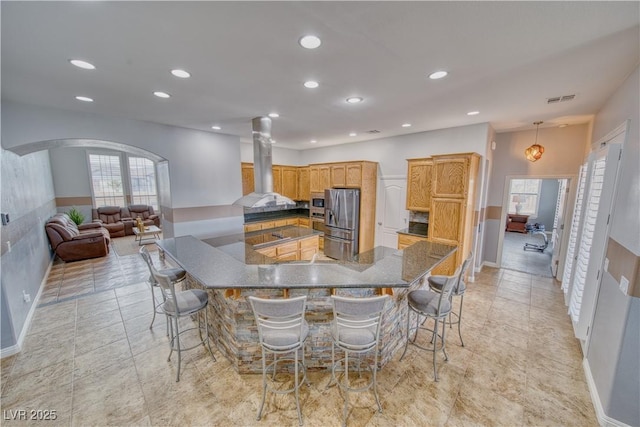 kitchen featuring pendant lighting, a breakfast bar area, stainless steel fridge, island exhaust hood, and kitchen peninsula