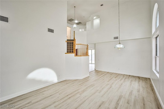 unfurnished living room featuring light wood-type flooring, plenty of natural light, and a high ceiling