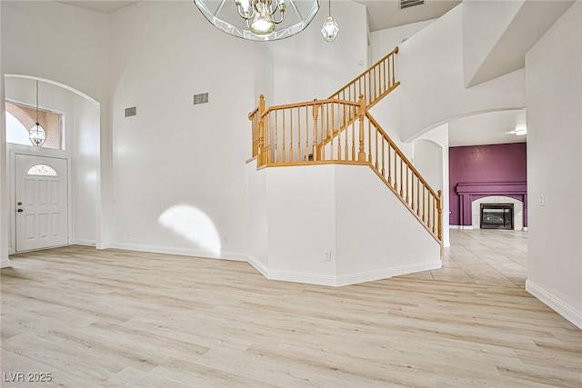 entryway with an inviting chandelier, a towering ceiling, a tiled fireplace, and light hardwood / wood-style flooring