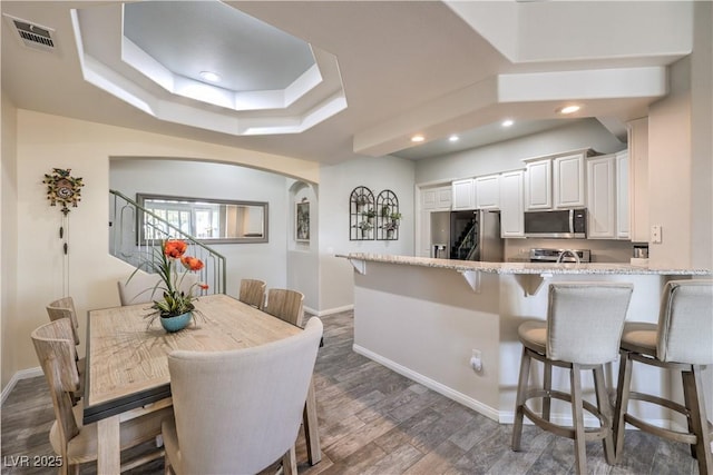 kitchen featuring a breakfast bar area, appliances with stainless steel finishes, a tray ceiling, light stone countertops, and white cabinets