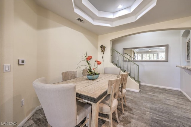 dining area with dark wood-type flooring and a tray ceiling