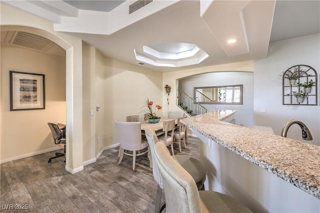 kitchen featuring light stone countertops, dark hardwood / wood-style floors, a kitchen breakfast bar, and a tray ceiling
