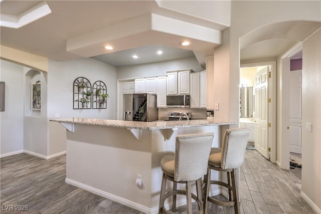 kitchen with appliances with stainless steel finishes, white cabinets, a kitchen breakfast bar, kitchen peninsula, and light stone countertops