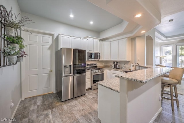 kitchen featuring appliances with stainless steel finishes, sink, white cabinets, a kitchen bar, and light stone countertops