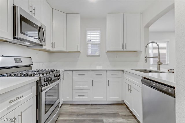 kitchen featuring white cabinetry, stainless steel appliances, sink, and light hardwood / wood-style flooring