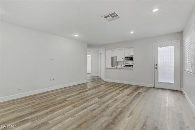 unfurnished living room featuring sink and light hardwood / wood-style flooring