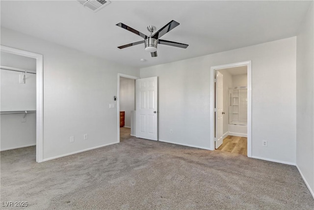 unfurnished bedroom with connected bathroom, a walk in closet, light carpet, a closet, and ceiling fan