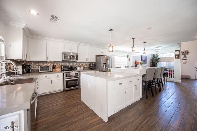 kitchen featuring appliances with stainless steel finishes, sink, white cabinets, hanging light fixtures, and a center island