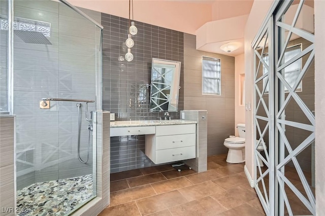 bathroom with vanity, toilet, a shower with door, and tile walls