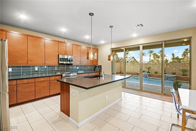 kitchen featuring sink, tasteful backsplash, decorative light fixtures, appliances with stainless steel finishes, and an island with sink