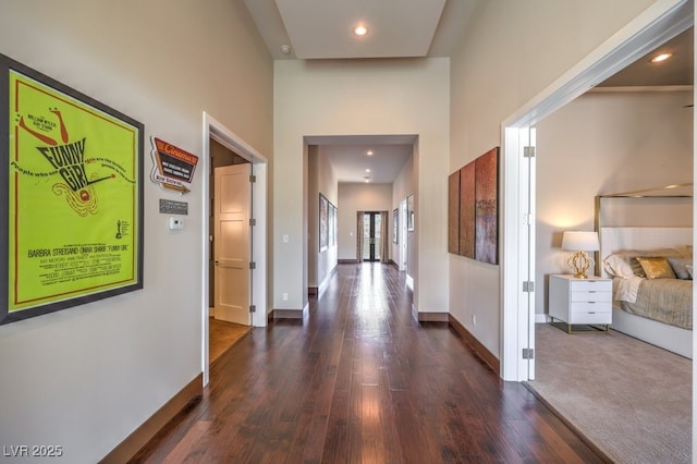 hallway featuring a towering ceiling and dark wood-type flooring