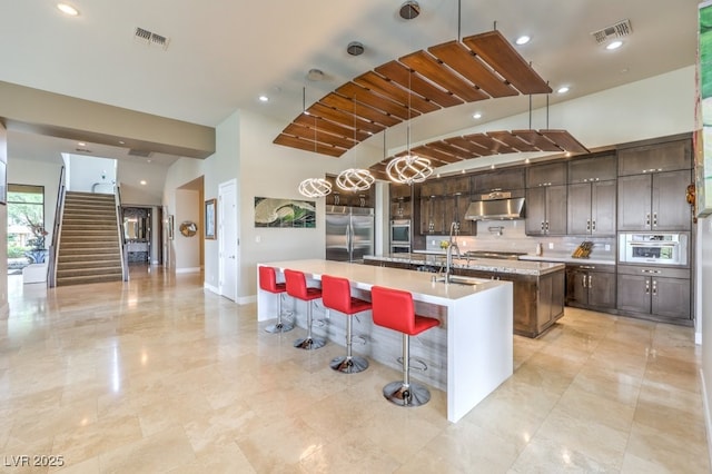 kitchen with a breakfast bar, sink, decorative backsplash, stainless steel appliances, and a center island with sink