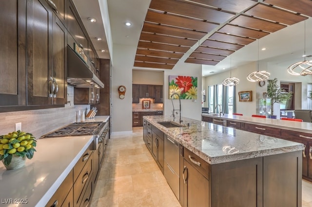 kitchen featuring decorative light fixtures, tasteful backsplash, sink, light stone countertops, and a center island with sink