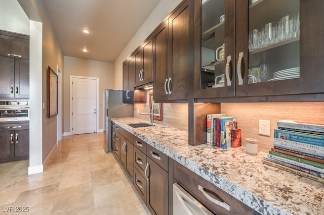 kitchen featuring sink, decorative backsplash, light stone counters, stainless steel appliances, and dark brown cabinets