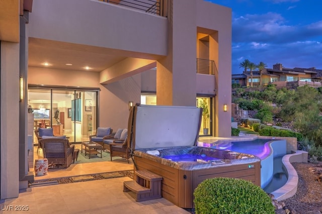 patio terrace at dusk featuring a hot tub, a balcony, and an outdoor hangout area