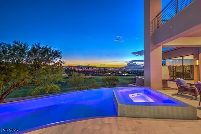 pool at dusk featuring an in ground hot tub and a patio