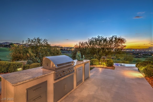 patio terrace at dusk featuring exterior kitchen and a grill