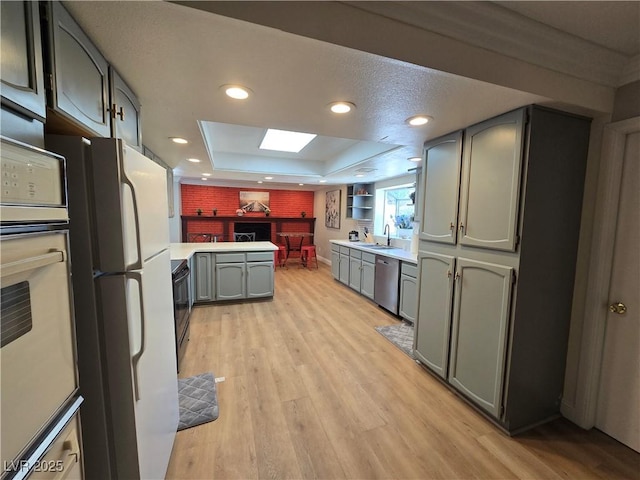 kitchen featuring a sink, white appliances, light wood-type flooring, and a raised ceiling