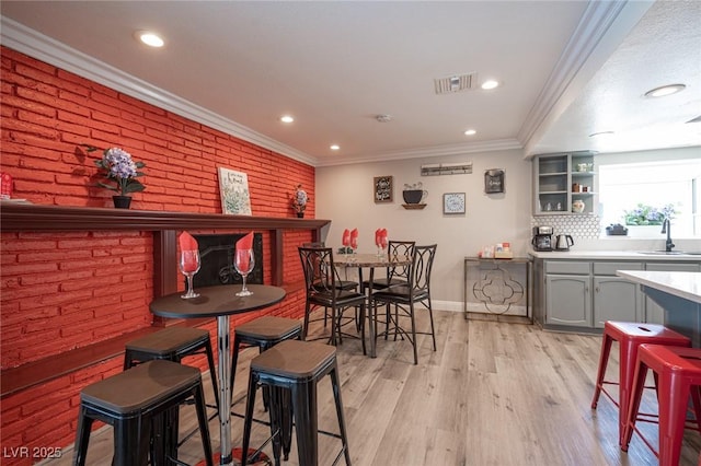 dining space featuring visible vents, ornamental molding, light wood-style floors, brick wall, and baseboards