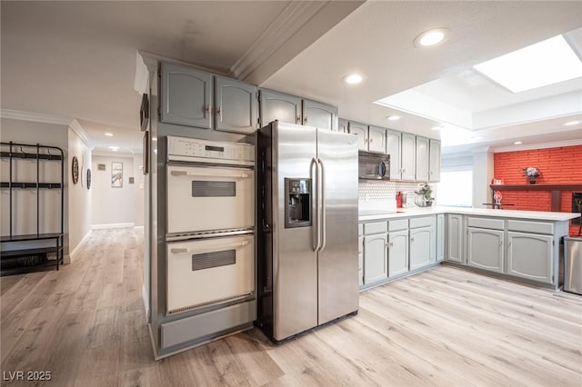 kitchen featuring a skylight, white double oven, stainless steel fridge with ice dispenser, light wood-style flooring, and crown molding