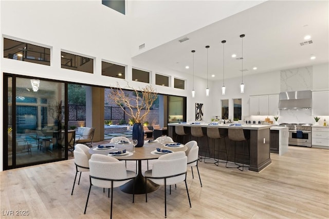 dining space featuring a towering ceiling and light hardwood / wood-style floors