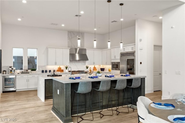 kitchen featuring wall chimney range hood, hanging light fixtures, a kitchen island with sink, and built in appliances