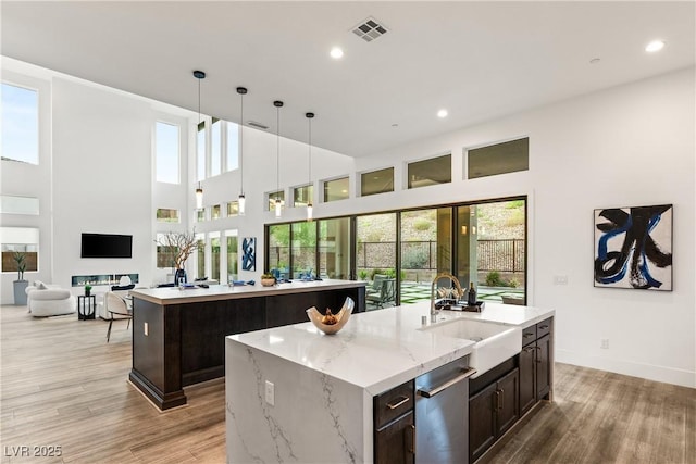 kitchen with sink, light hardwood / wood-style flooring, hanging light fixtures, light stone countertops, and a center island with sink