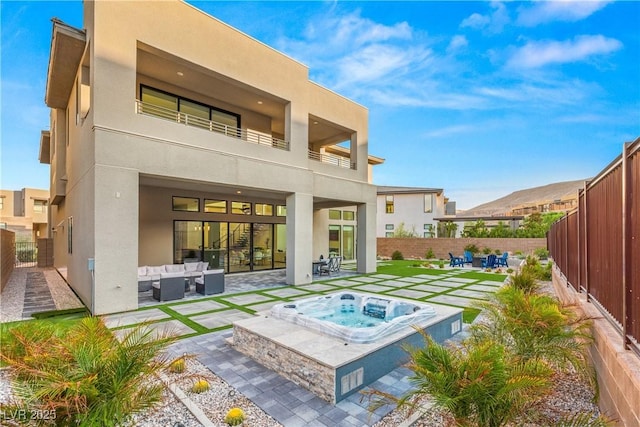 rear view of property featuring an outdoor hot tub, an outdoor living space, a mountain view, and a patio