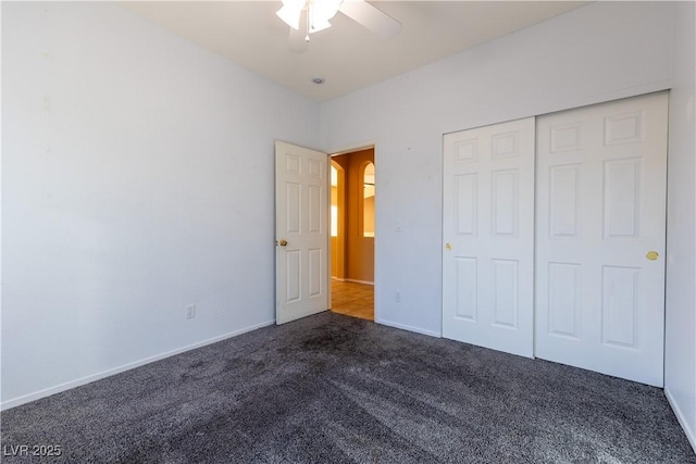 unfurnished bedroom with ceiling fan, dark carpet, and a closet