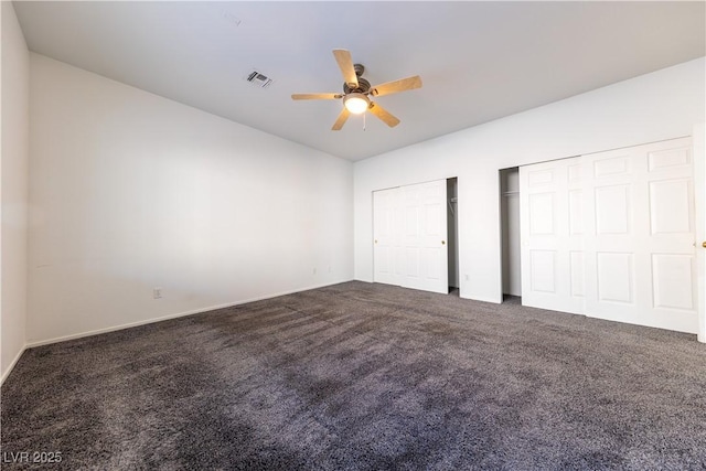 unfurnished bedroom with two closets, ceiling fan, and dark colored carpet