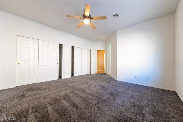 unfurnished bedroom featuring ceiling fan, dark carpet, and two closets