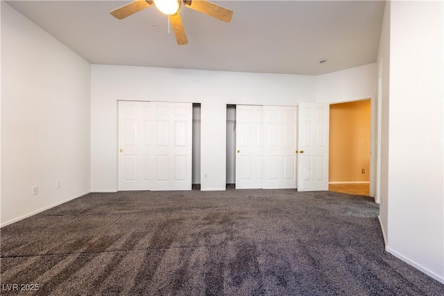 unfurnished bedroom featuring ceiling fan, multiple closets, and dark colored carpet