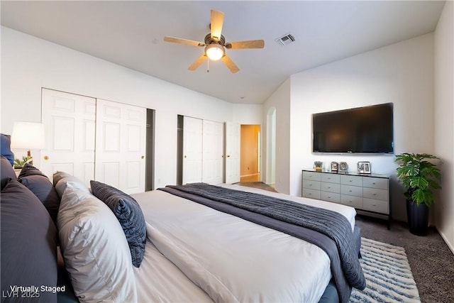 bedroom with ceiling fan, two closets, and dark carpet